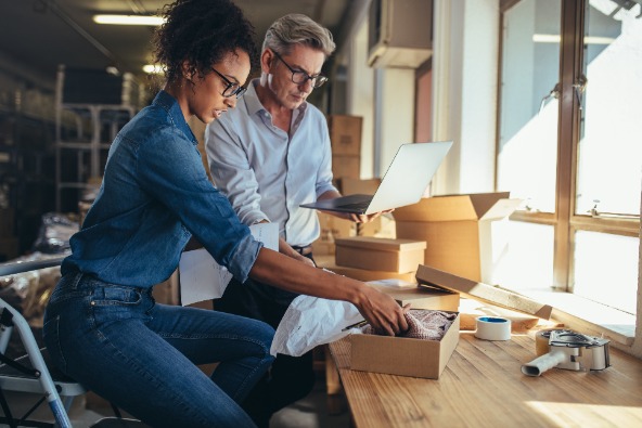 A young black woman and older Caucasian man work together to organise clothing orders